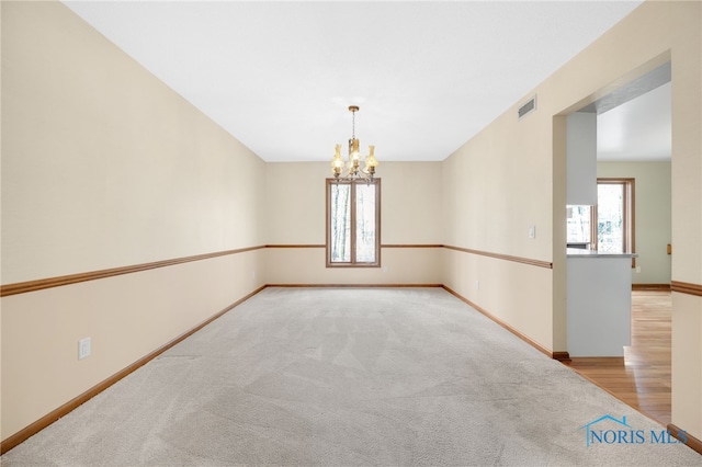 carpeted empty room featuring a healthy amount of sunlight, baseboards, visible vents, and a notable chandelier