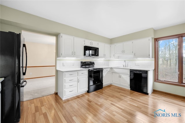 kitchen featuring a sink, light wood-style floors, light countertops, black appliances, and tasteful backsplash