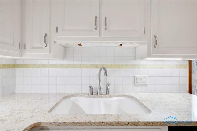 details featuring light stone counters, white cabinetry, decorative backsplash, and a sink