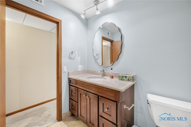 bathroom featuring toilet, rail lighting, vanity, and baseboards