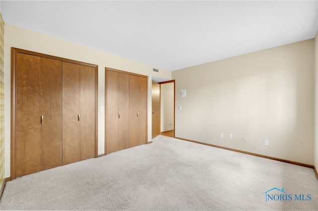 unfurnished bedroom featuring carpet, visible vents, baseboards, and two closets