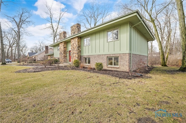 view of front of house with board and batten siding, a front yard, brick siding, and a chimney