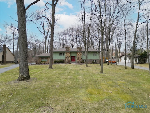 view of front of home with stone siding, a chimney, a front lawn, and board and batten siding