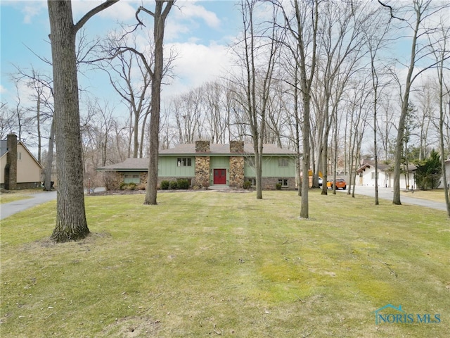 view of front of house featuring stone siding, a chimney, a front lawn, and board and batten siding