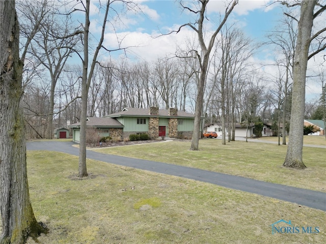 view of front of property with a garage, aphalt driveway, a chimney, and a front lawn