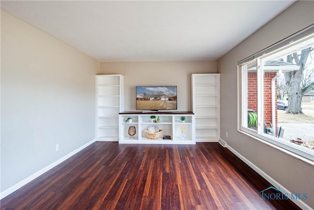 unfurnished living room with plenty of natural light, wood finished floors, and baseboards