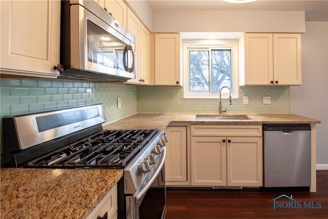 kitchen with stainless steel appliances, dark wood-type flooring, a sink, and light stone counters