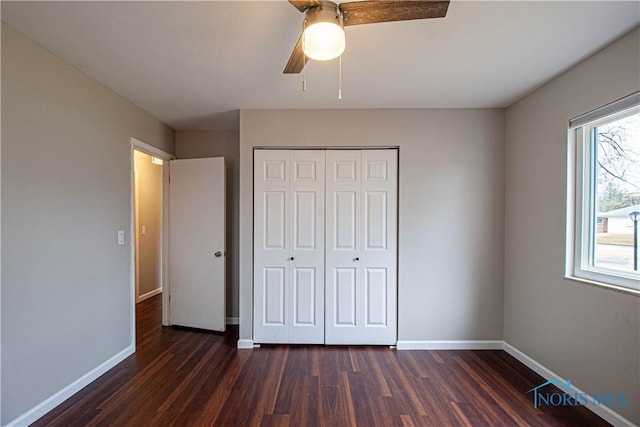 unfurnished bedroom featuring baseboards, dark wood finished floors, and a closet