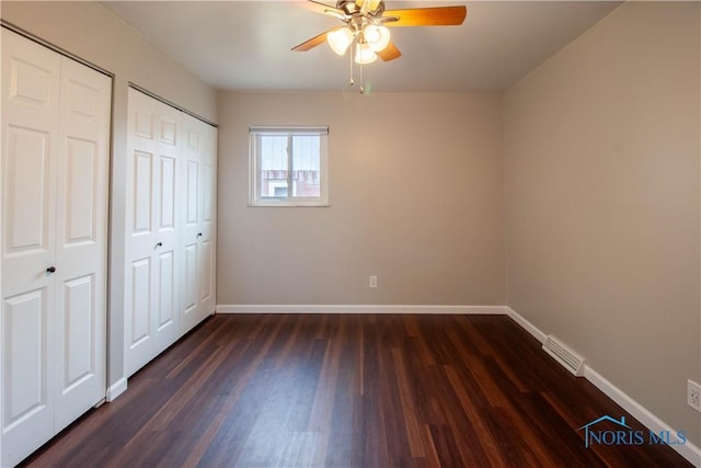 unfurnished bedroom featuring baseboards, dark wood-type flooring, and two closets