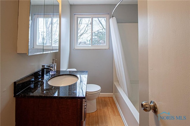 full bath featuring toilet, shower / bath combo, vanity, wood finished floors, and baseboards