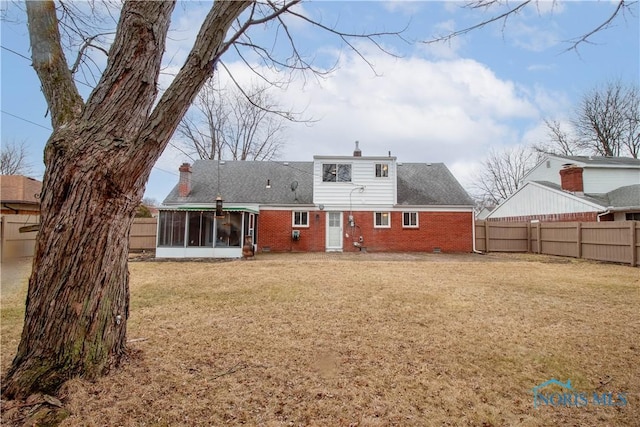 back of property featuring fence private yard, brick siding, a sunroom, a yard, and a chimney