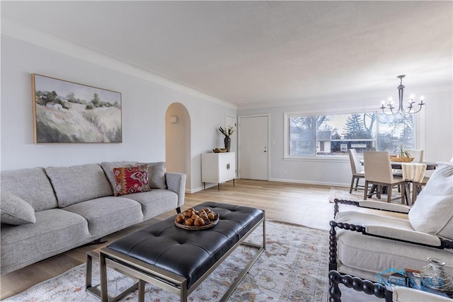 living area featuring arched walkways, light wood-type flooring, baseboards, and an inviting chandelier