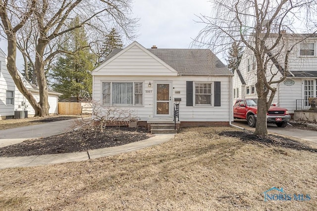 bungalow-style house with cooling unit, fence, roof with shingles, a chimney, and concrete driveway