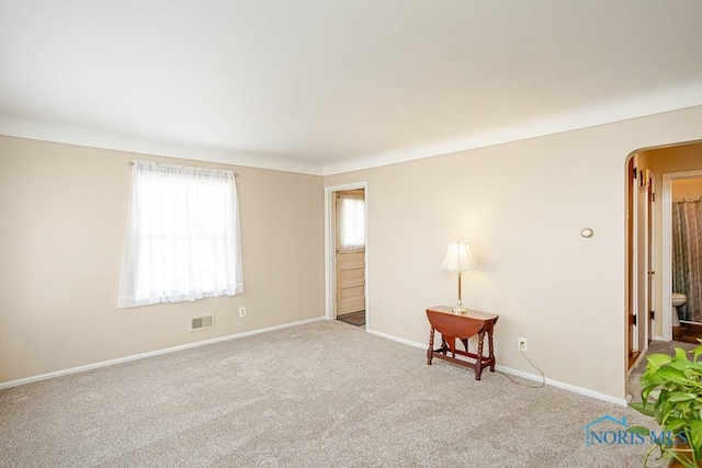 unfurnished room featuring carpet flooring, visible vents, arched walkways, and baseboards