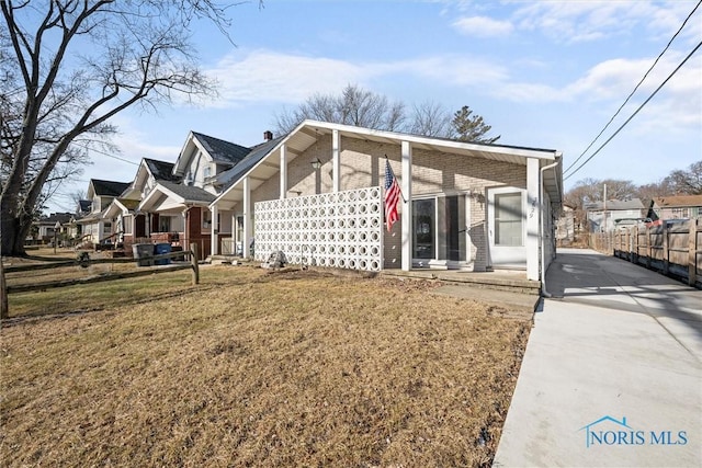 view of front of property featuring brick siding, a front lawn, fence, and a residential view