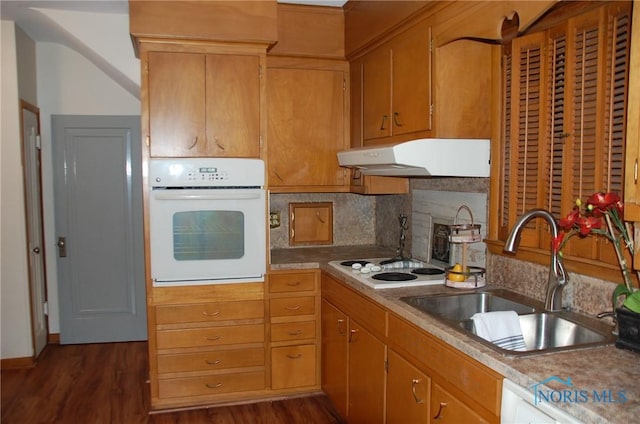 kitchen with under cabinet range hood, white appliances, dark wood-style flooring, a sink, and backsplash