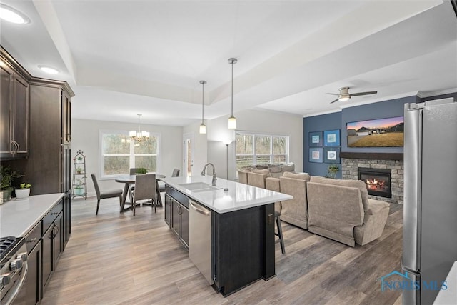 kitchen with a raised ceiling, light countertops, dark brown cabinets, stainless steel appliances, and a sink