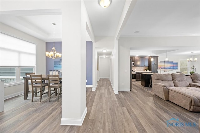 living area with baseboards, a tray ceiling, light wood-style floors, and a notable chandelier