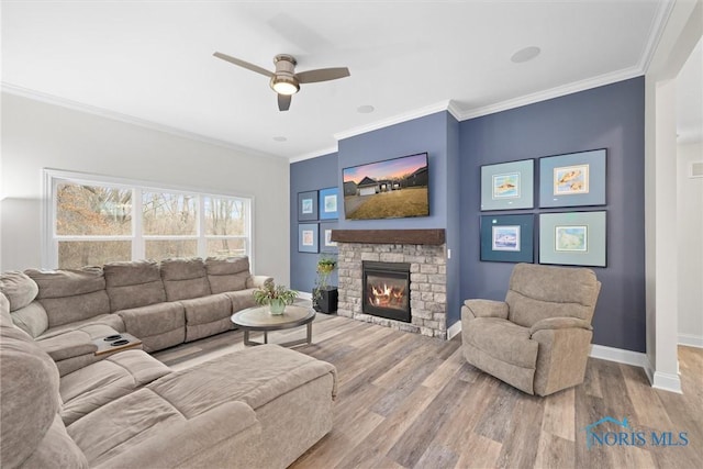 living area featuring baseboards, a ceiling fan, ornamental molding, wood finished floors, and a stone fireplace