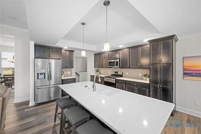 kitchen featuring a breakfast bar, a sink, dark brown cabinets, appliances with stainless steel finishes, and a raised ceiling