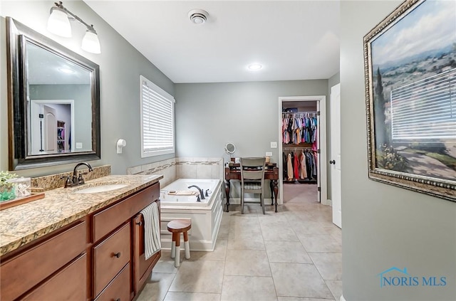 bathroom with a spacious closet, a garden tub, vanity, and tile patterned floors