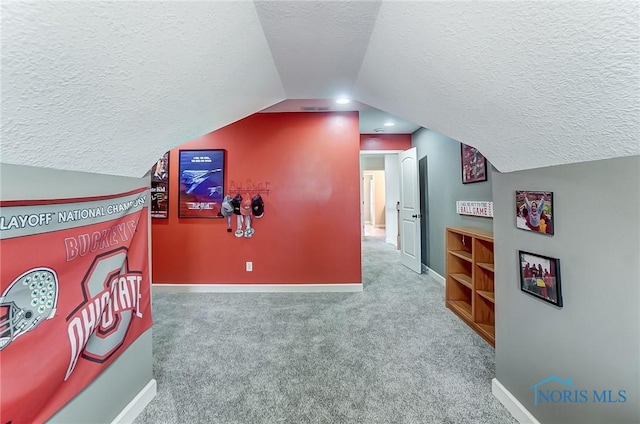 interior space with visible vents, carpet flooring, vaulted ceiling, a textured ceiling, and baseboards