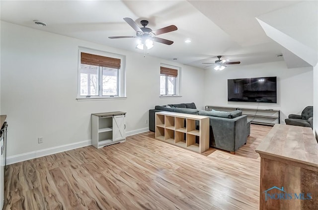 living room featuring a ceiling fan, baseboards, and light wood finished floors