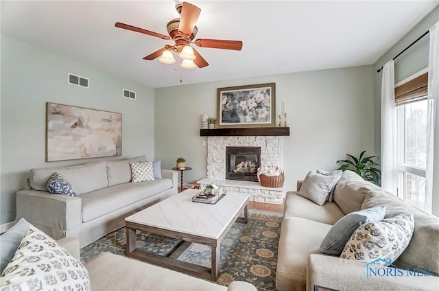 living room with a fireplace, visible vents, and a ceiling fan