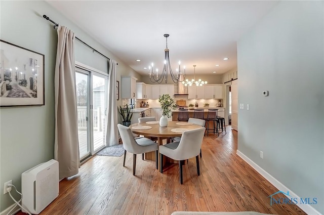 dining space with a barn door, baseboards, light wood-style flooring, a notable chandelier, and recessed lighting