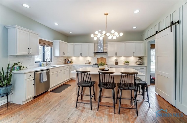 kitchen with a barn door, a breakfast bar, wall chimney range hood, a center island, and dishwasher