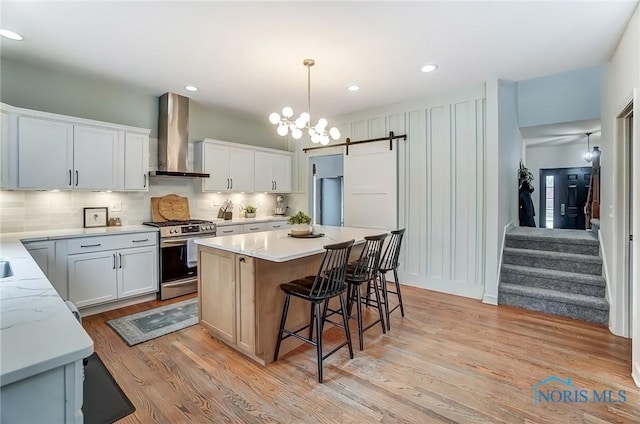 kitchen featuring a barn door, a kitchen island, stainless steel gas range, wall chimney range hood, and backsplash