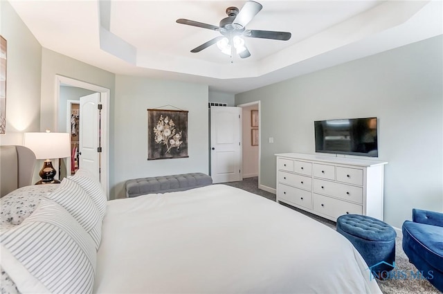 bedroom with a tray ceiling, carpet flooring, a ceiling fan, and baseboards