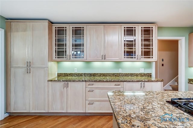 kitchen with black gas cooktop, glass insert cabinets, light wood-style flooring, and light stone countertops