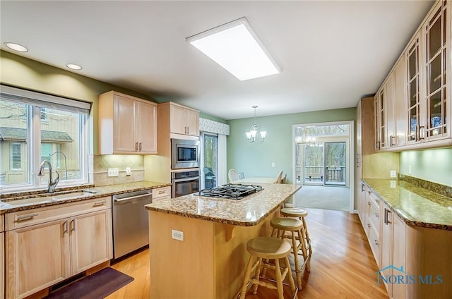 kitchen featuring glass insert cabinets, appliances with stainless steel finishes, light stone counters, a center island, and a sink