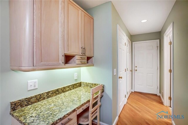 kitchen featuring baseboards, light wood-type flooring, light stone countertops, light brown cabinetry, and built in desk