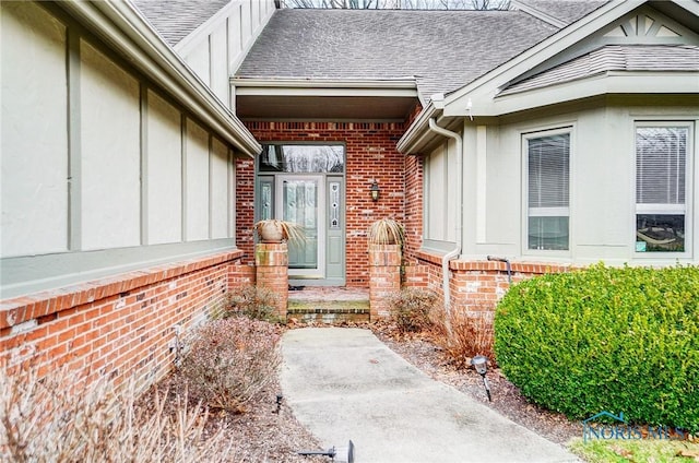 entrance to property featuring roof with shingles and brick siding