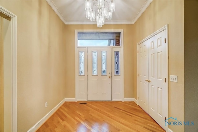 foyer featuring light wood-type flooring, a notable chandelier, baseboards, and crown molding