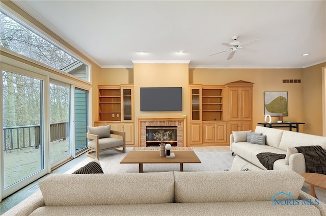 living area with a ceiling fan, visible vents, ornamental molding, and a tiled fireplace