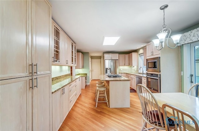 kitchen featuring a center island, light wood finished floors, appliances with stainless steel finishes, glass insert cabinets, and a sink