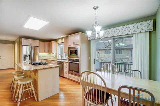 kitchen featuring light wood finished floors, a kitchen island, a breakfast bar area, light stone countertops, and stainless steel appliances