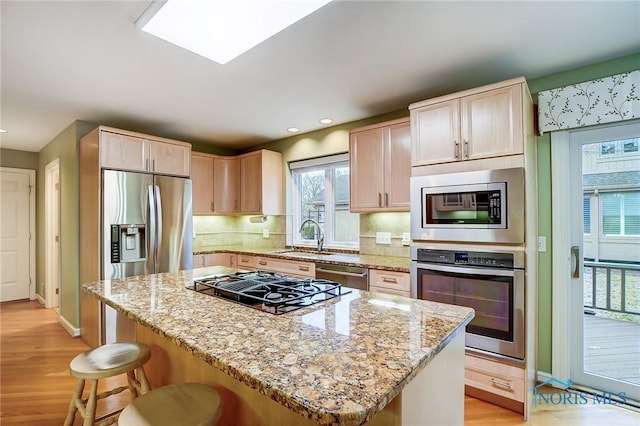 kitchen featuring decorative backsplash, a kitchen island, stainless steel appliances, light wood-type flooring, and a sink