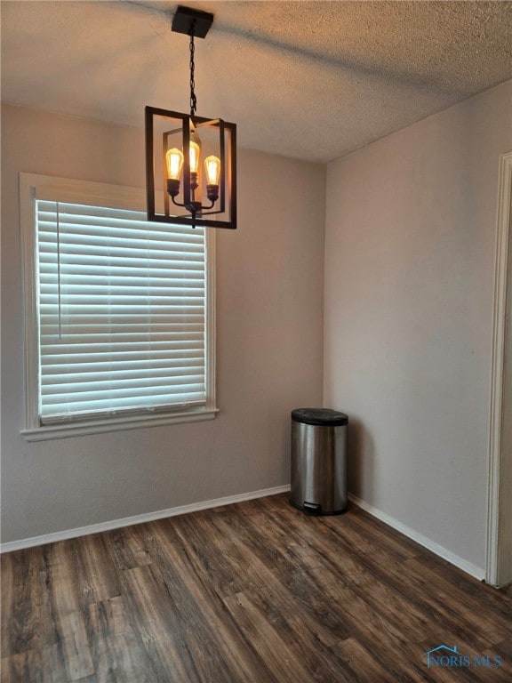 unfurnished room featuring baseboards, dark wood-type flooring, a textured ceiling, and an inviting chandelier