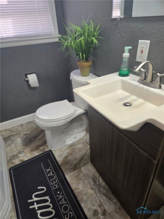 half bath with baseboards, vanity, and toilet