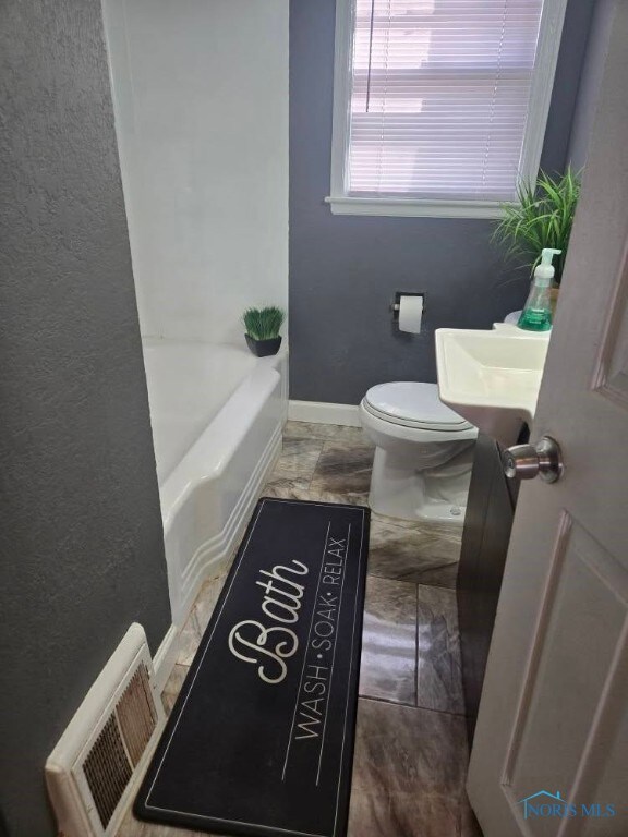 full bath featuring a textured wall, toilet, visible vents, baseboards, and a bath