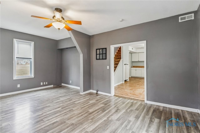 spare room with stairway, wood finished floors, visible vents, baseboards, and arched walkways