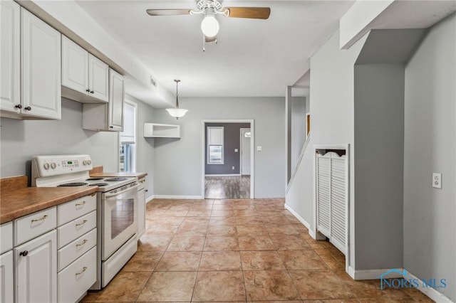 kitchen with light tile patterned floors, a ceiling fan, white range with electric cooktop, hanging light fixtures, and white cabinetry