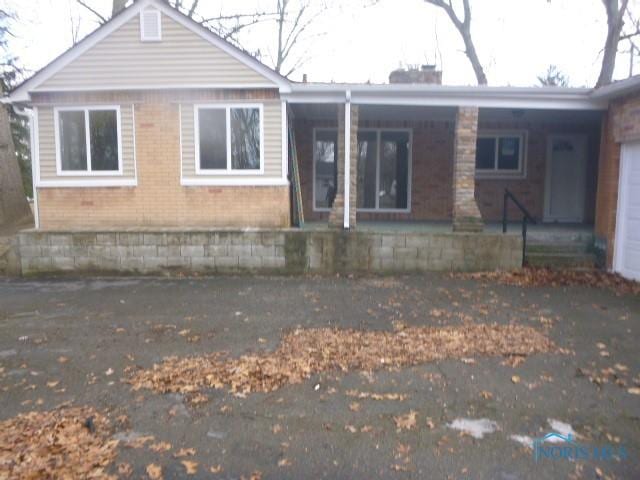 rear view of property with a garage, covered porch, a chimney, and brick siding