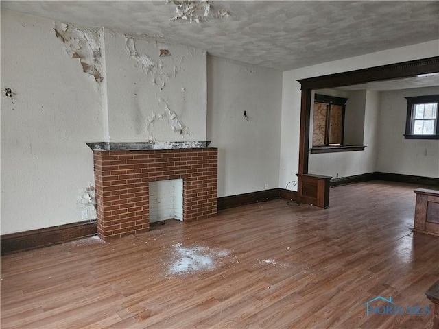 unfurnished living room with a brick fireplace, baseboards, and wood finished floors