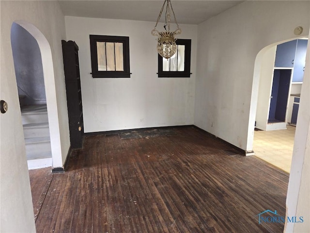 empty room with arched walkways, baseboards, and wood finished floors