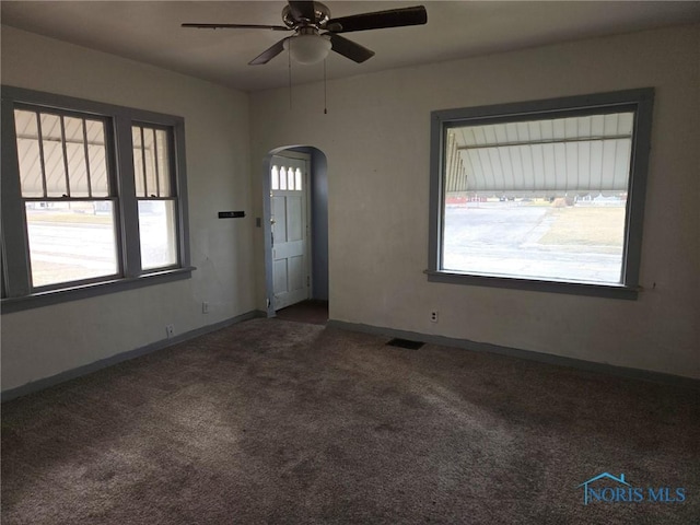 carpeted empty room with a ceiling fan, arched walkways, visible vents, and baseboards